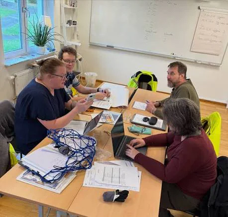Fyra personer samarbetar vid ett bord med datorer och dokument