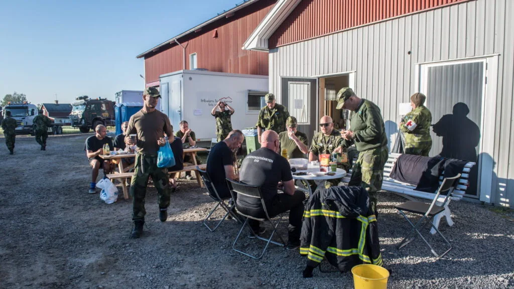Frivilliga och uniformerade deltagare samlade vid bord utanför en byggnad